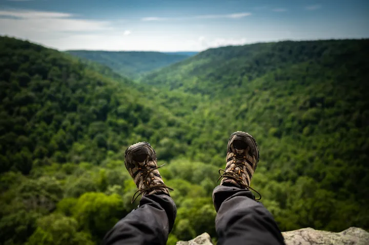 Hiking boots dangling over a cliff edge overlooking green Tennessee hills