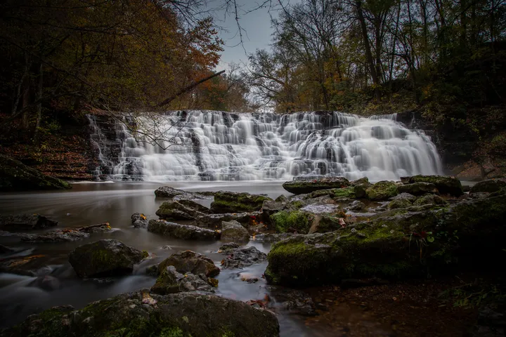 Wide cascading falls rushing over mossy rocks into a still pool
