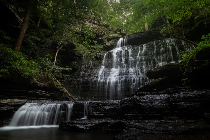 Waterfall splitting over dark rock into a shadowed pool below