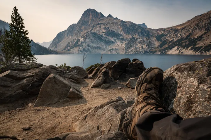 Hiking boots resting on rocks overlooking an alpine lake and mountain peak